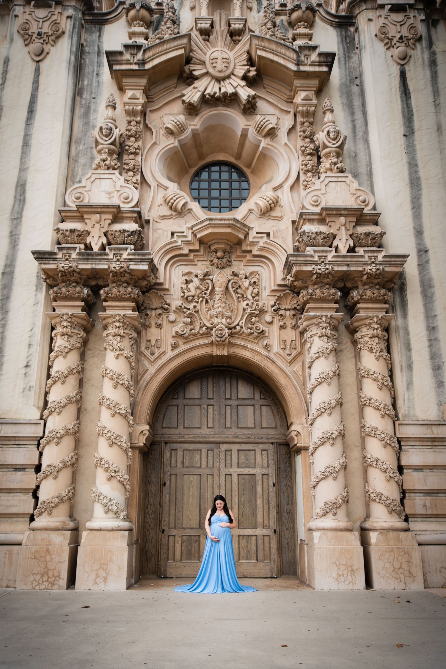 Elegant maternity photos at ornate baroque church facade with blue flowing dress.