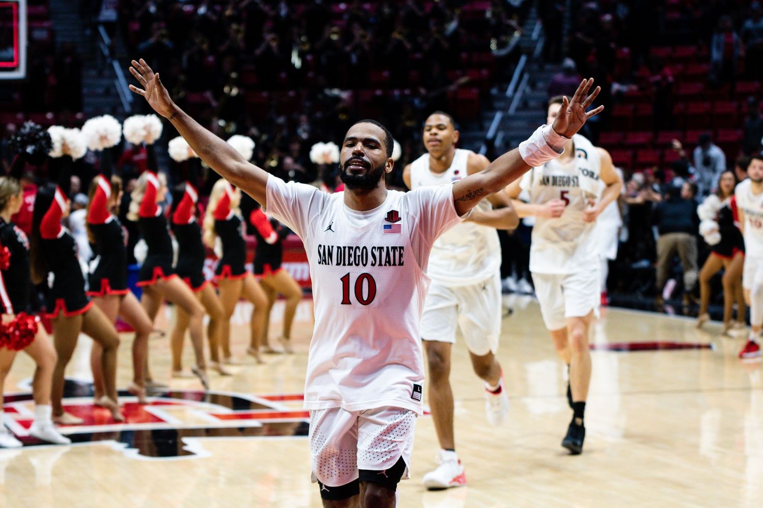 San Diego State basketball player #10 celebrates with arms raised after a home game win.