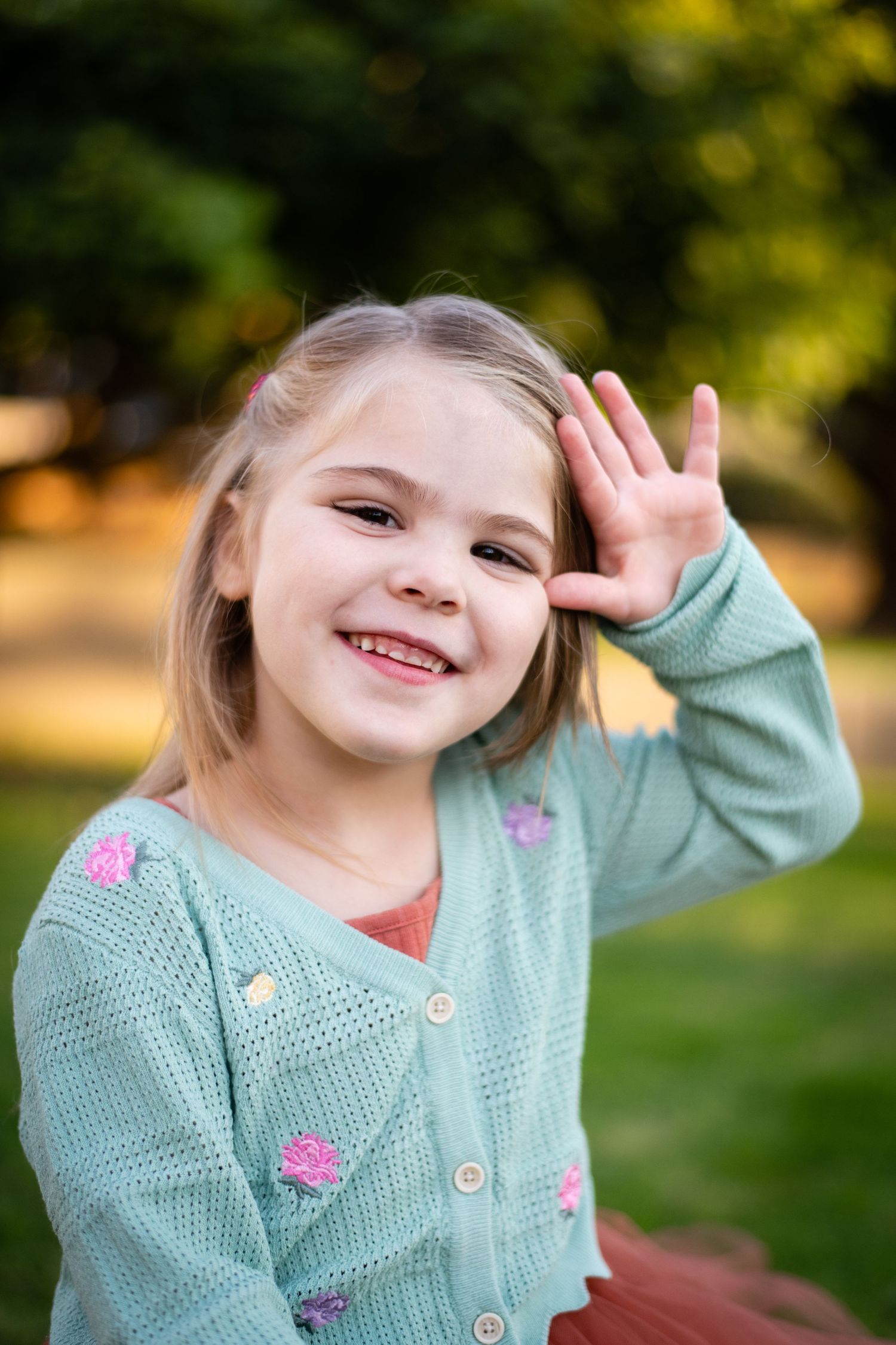 Child in mint green cardigan making playful expressions outdoors.