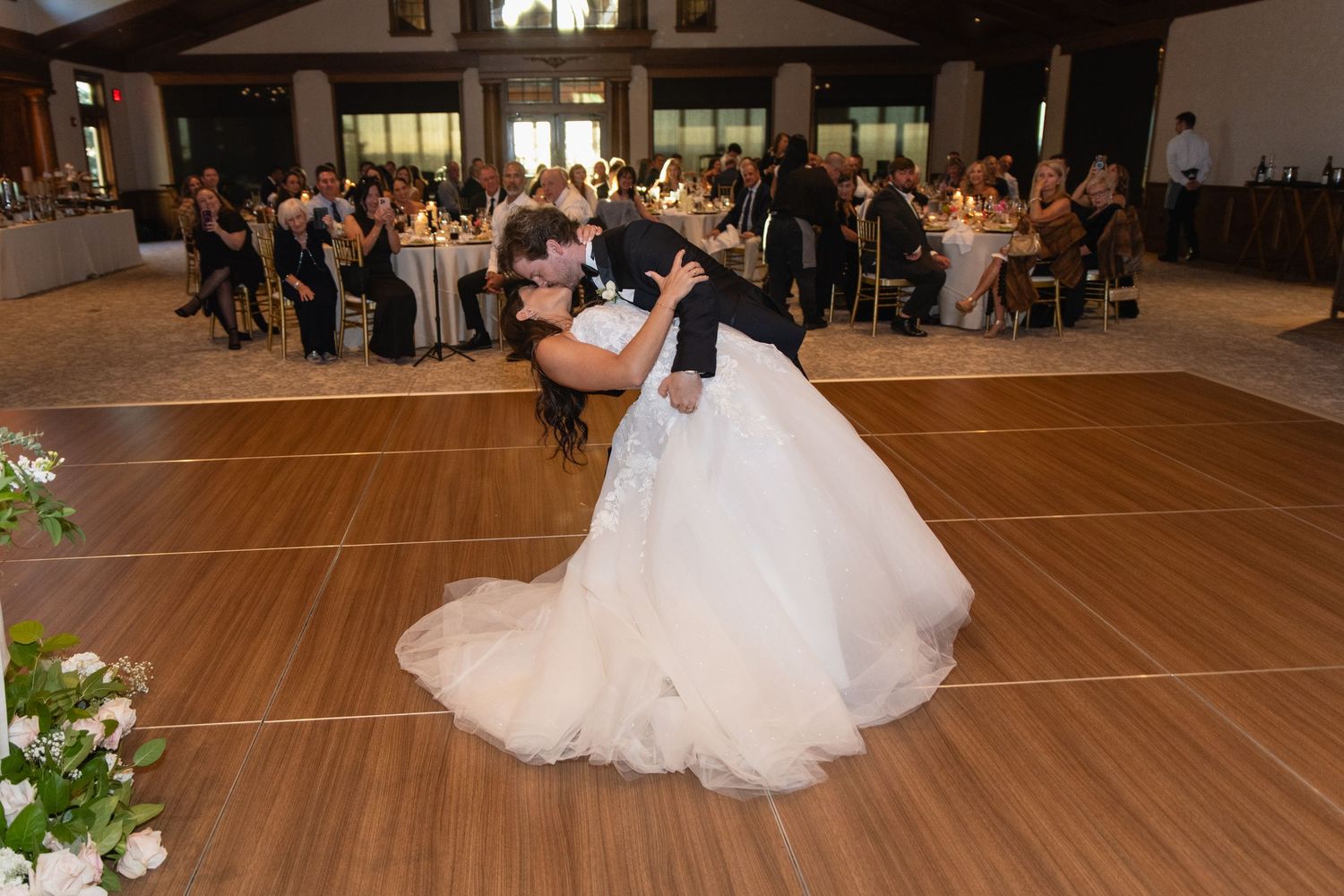 Dancers glide across a polished wooden dance floor during a wedding reception in an elegant venue.