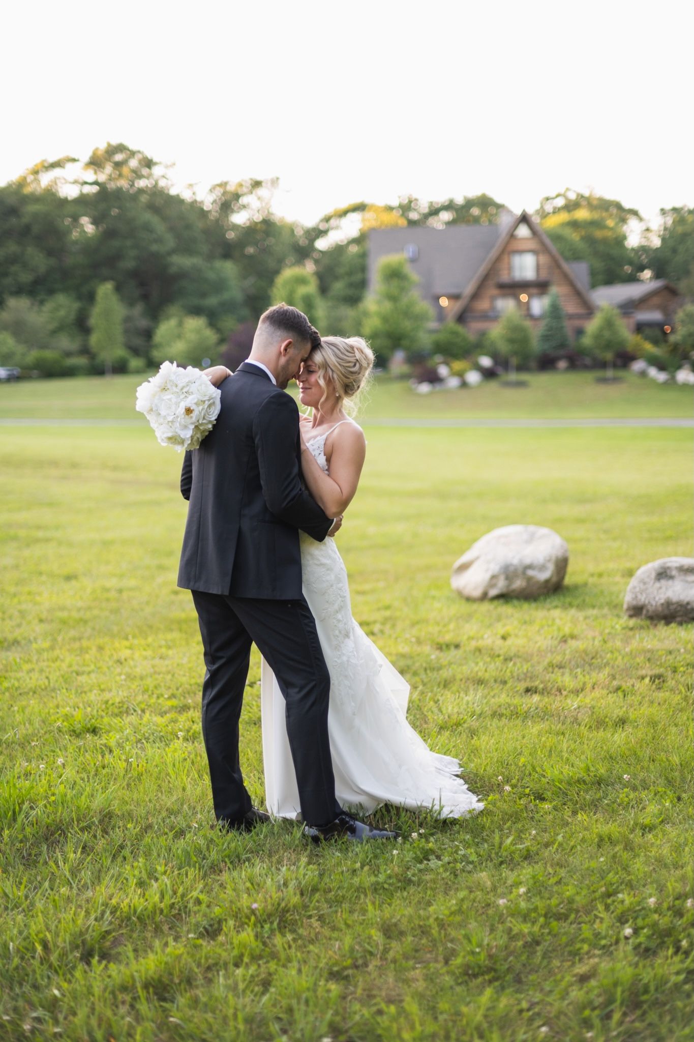Romantic sunset wedding portraits of couple in an open field with houses in background.