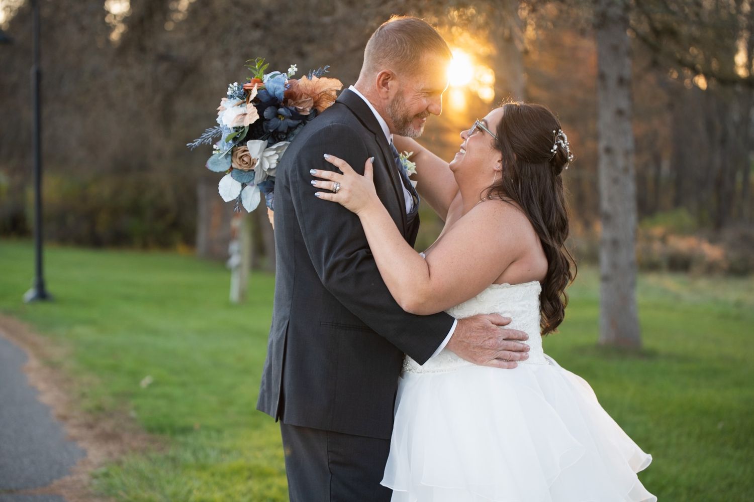 A romantic sunset wedding photo of newlyweds kissing outdoors with a bouquet.