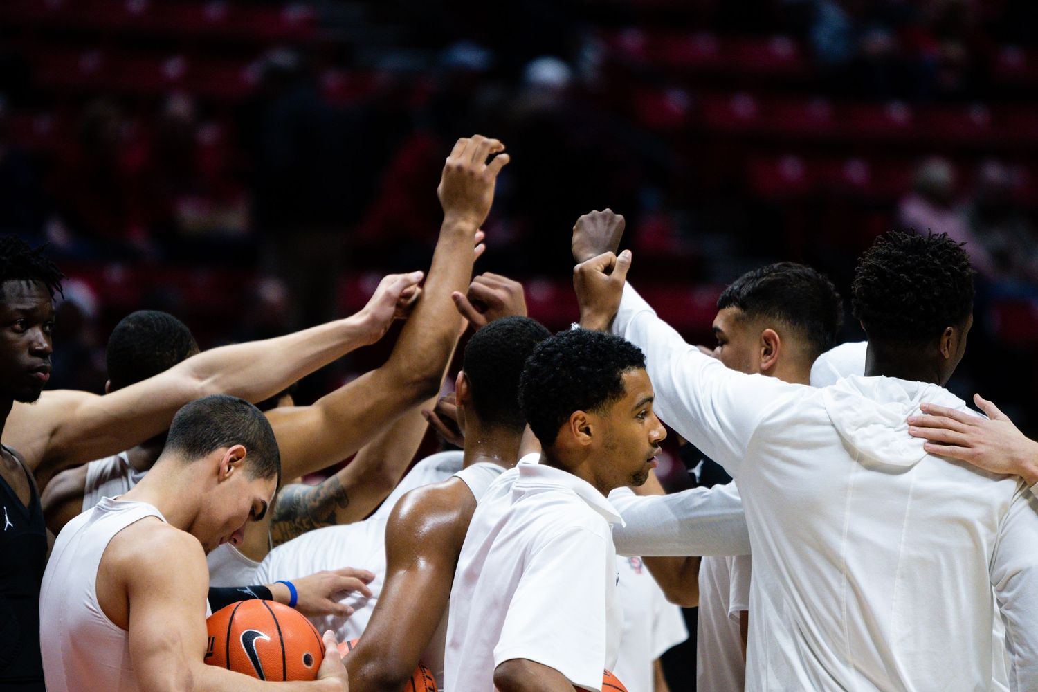 College basketball team huddles together, raising hands in unity before a game on the court.