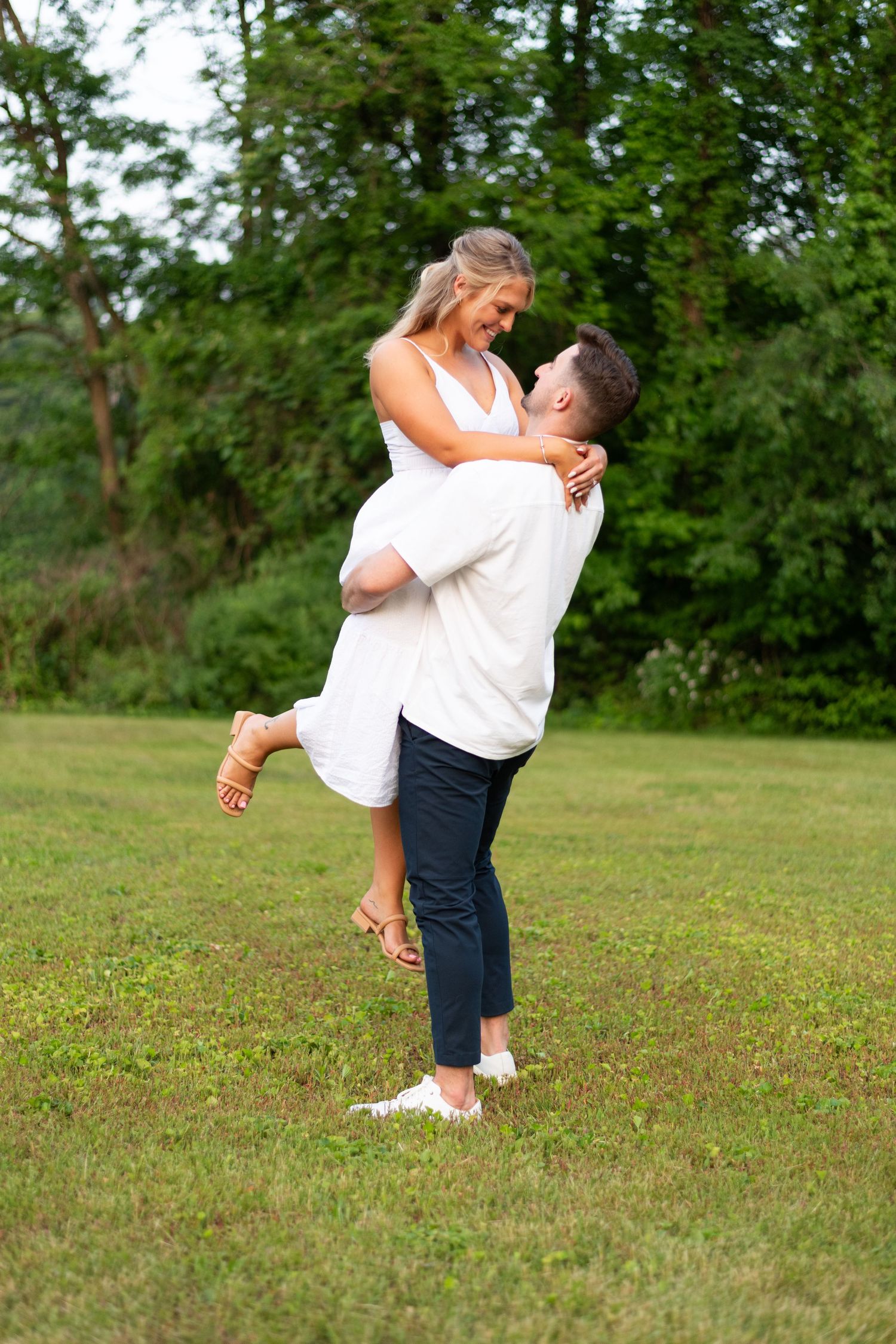 A romantic outdoor photoshoot series showing a couple in white and navy outfits embracing in a grassy field.