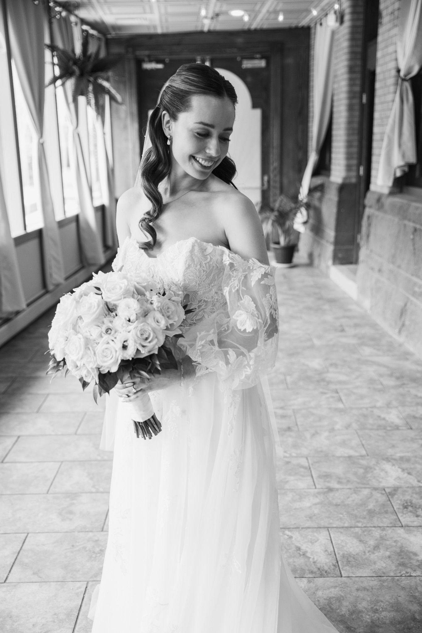 Black and white portrait showcasing elegant bridal bouquet and lace wedding gown details.