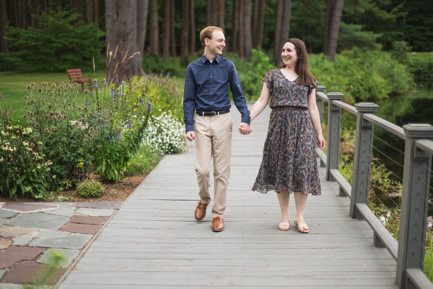 Couple walking along wooden boardwalk path surrounded by lush garden scenery.