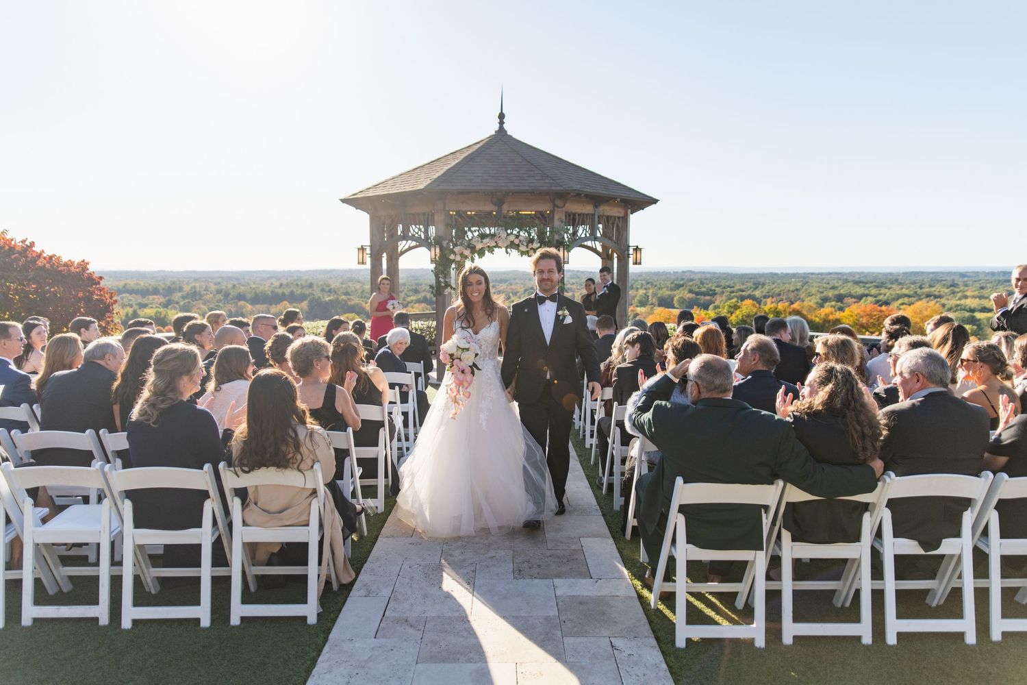 Wedding ceremony setup with white chairs overlooking a scenic mountain landscape at sunset.