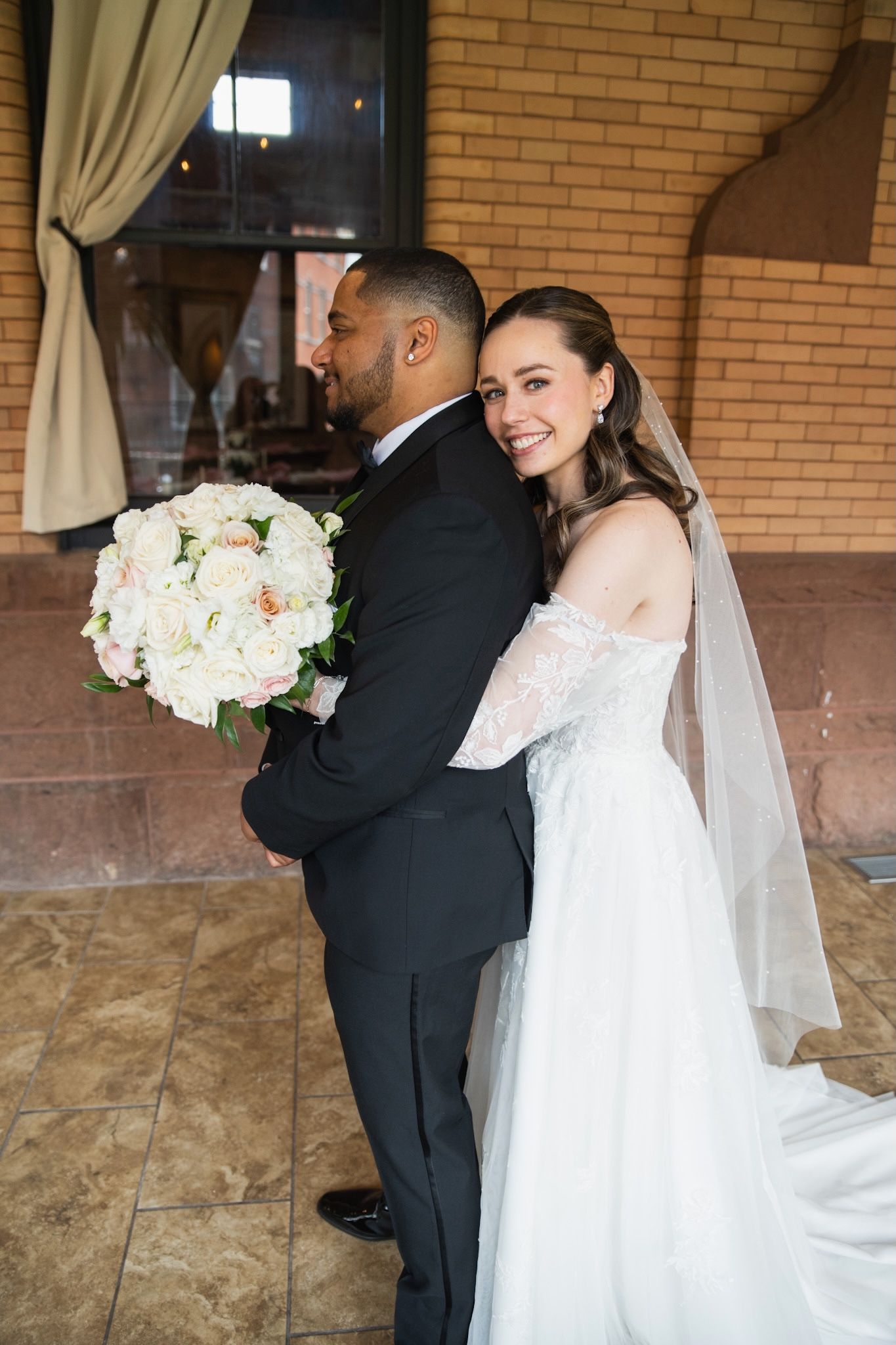 Candid wedding moments captured against warm brick walls with elegant floral bouquets.