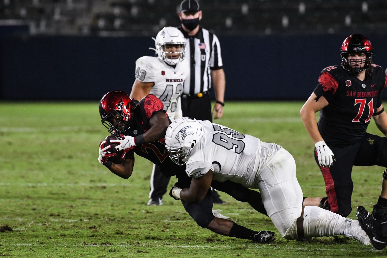 San Diego State football player carries the ball while being tackled during a night game.