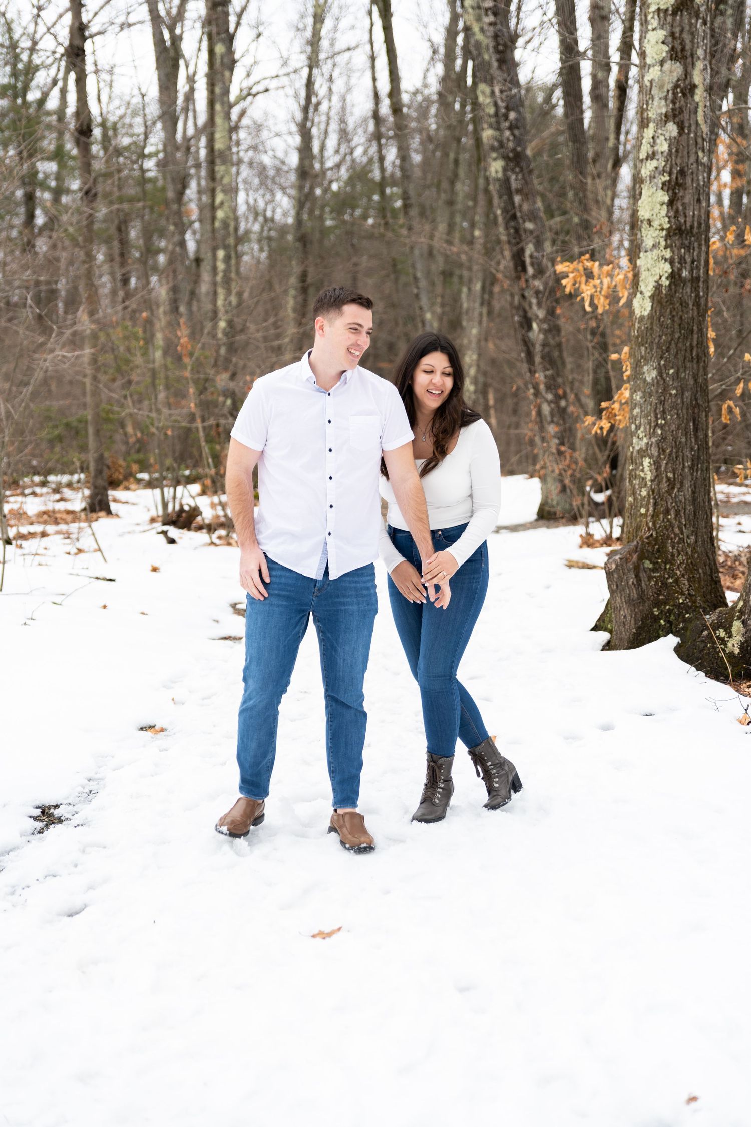 Playful couple posing in a snowy winter forest setting.