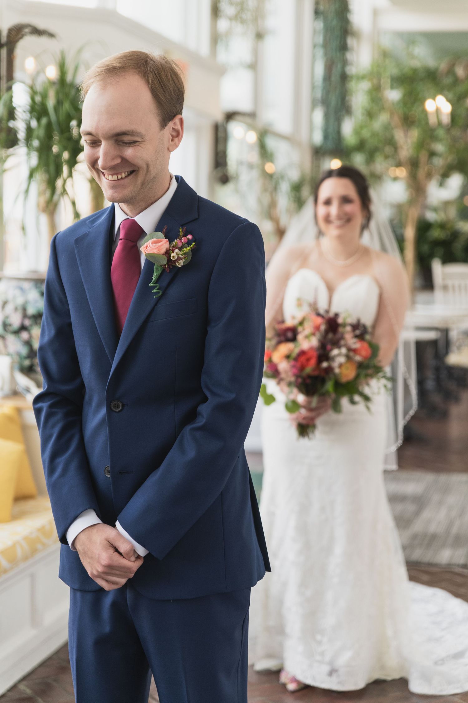 Wedding party members in navy suits and white dresses share emotional first look moments in an outdoor setting.