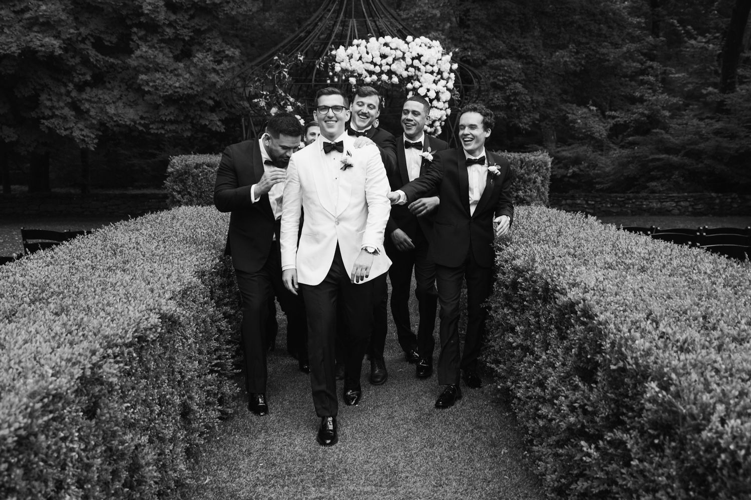 Wedding party walking along garden path in formal black and white attire.