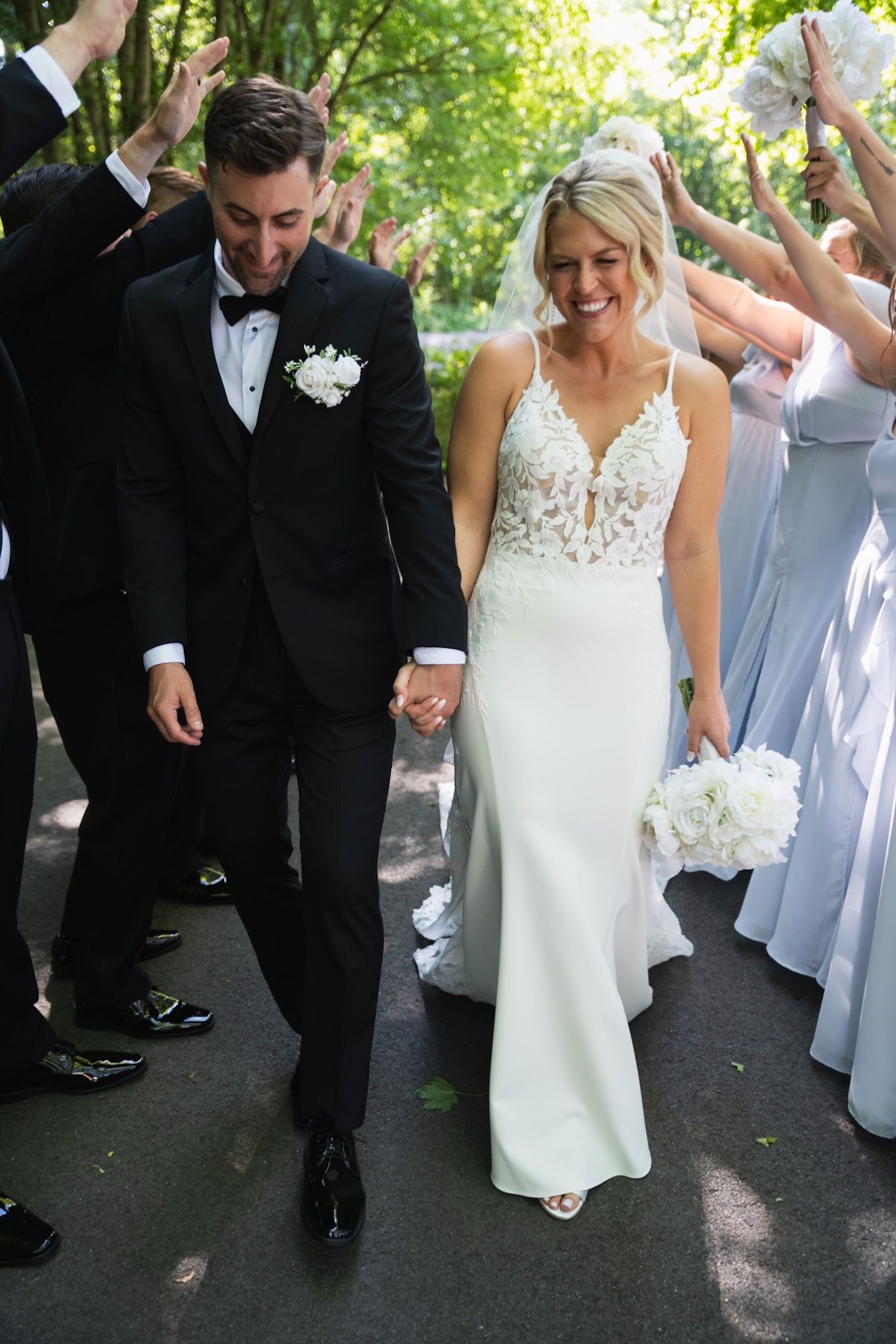Wedding party walks together outdoors celebrating with raised arms and joyful expressions.