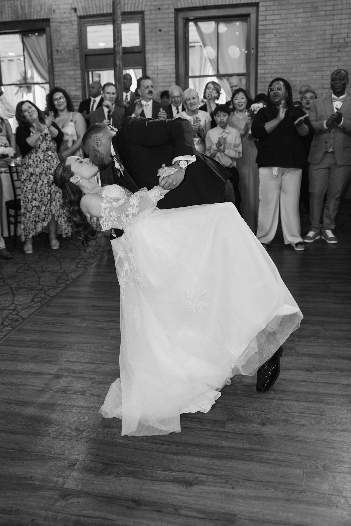 Couple dancing with flowing white dress spinning on wooden dance floor surrounded by guests.