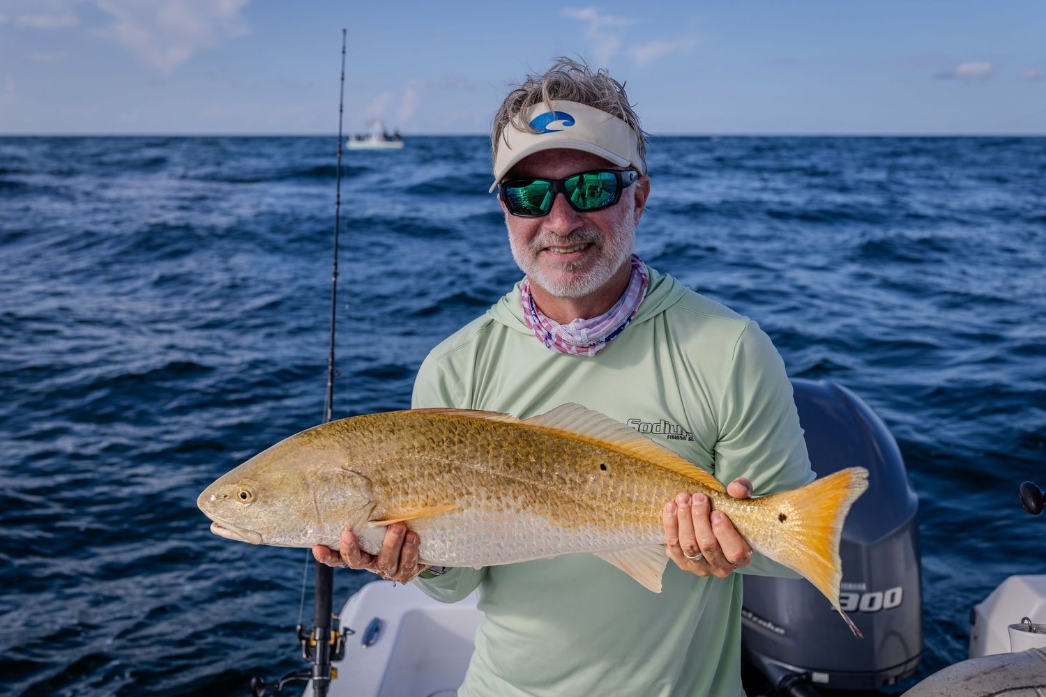 An angler holds a large red drum aboard a fishing boat on choppy blue water.