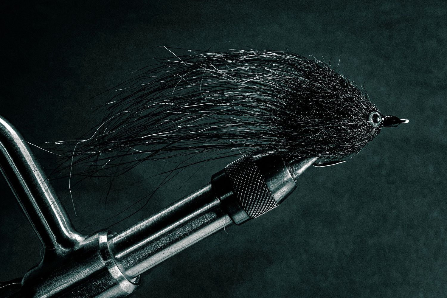 Black fly, monochrome treatment
Macro photograph of a hand-tied black saltwater fly secured in a fly-tying vise, emphasizing feather texture