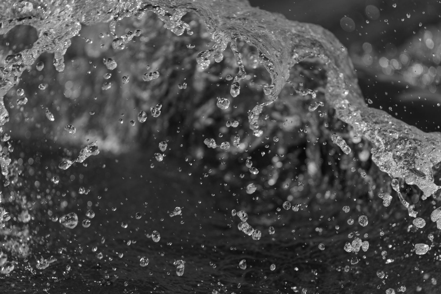 A breaking wave curls into bright droplets in a close black-and-white study.