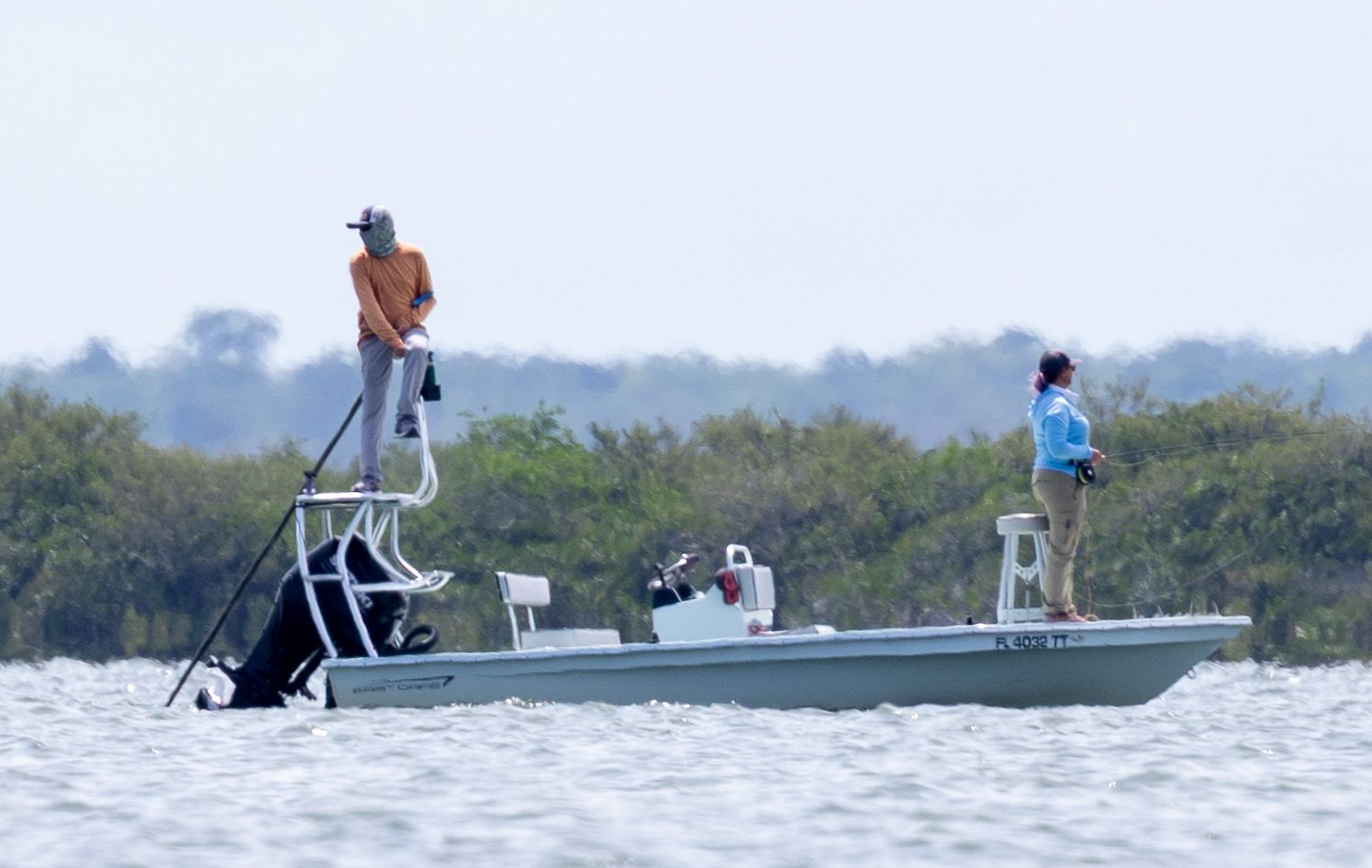 A guide poles a flats skiff while an angler casts across choppy water.