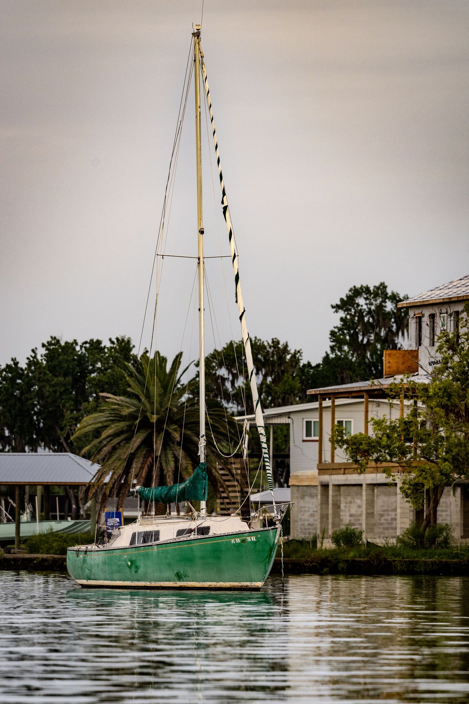 Green sailboat anchored near waterfront homes and palm trees on Kings Bay in Crystal River.