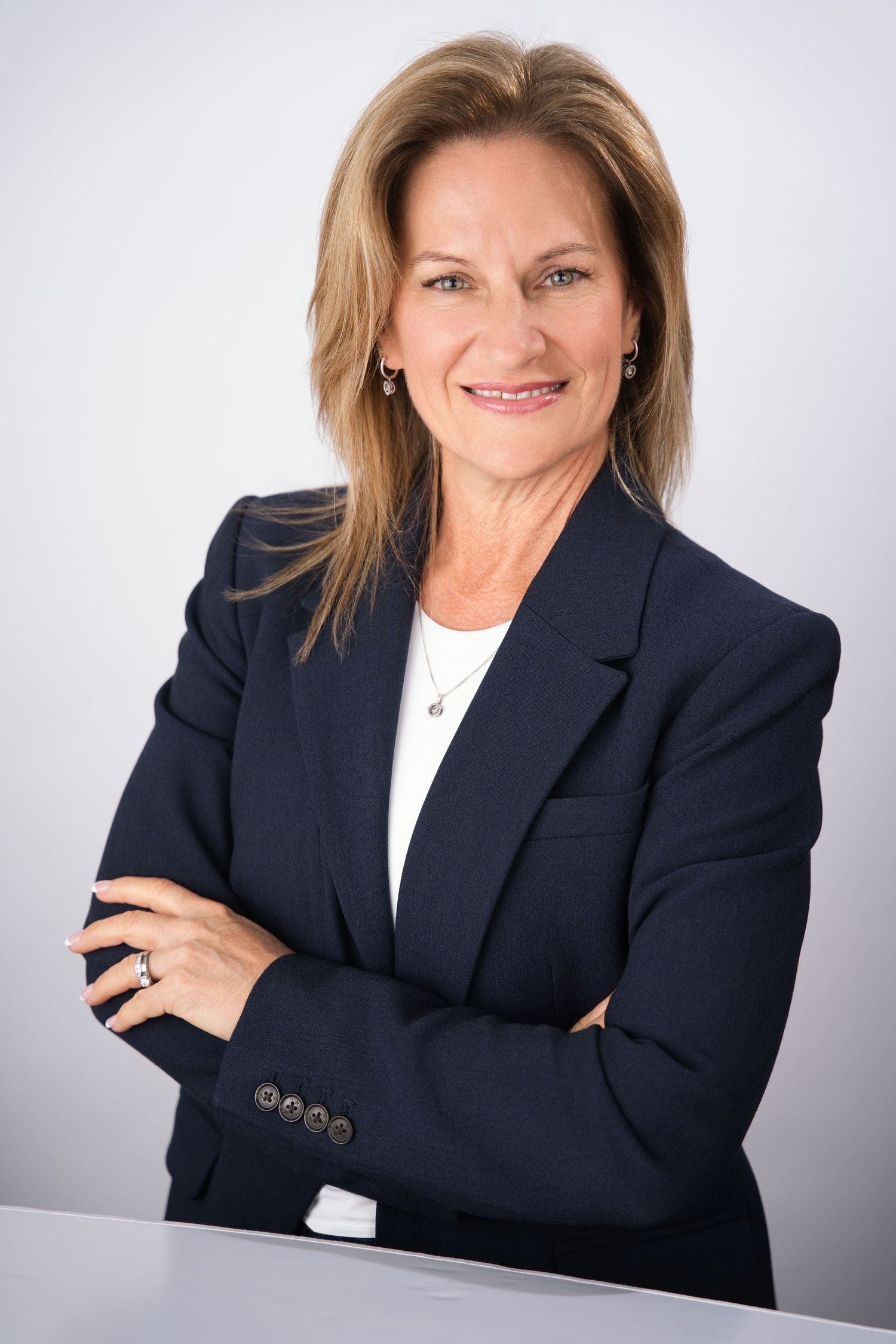 Confident businesswoman in navy blazer with arms crossed smiling against a light grey studio background.