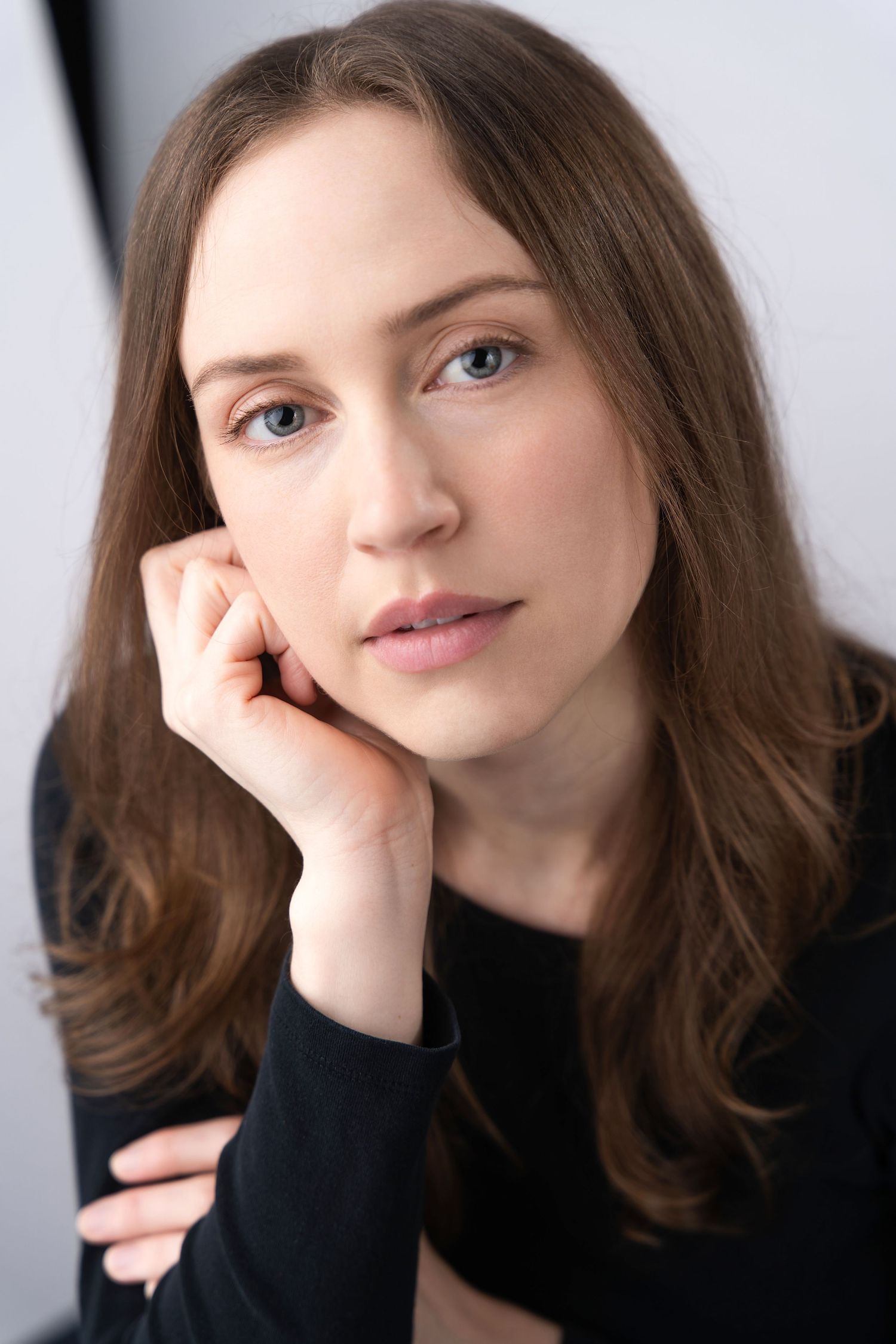 Portrait of a young brunette woman resting her chin on her hand wearing a black top.