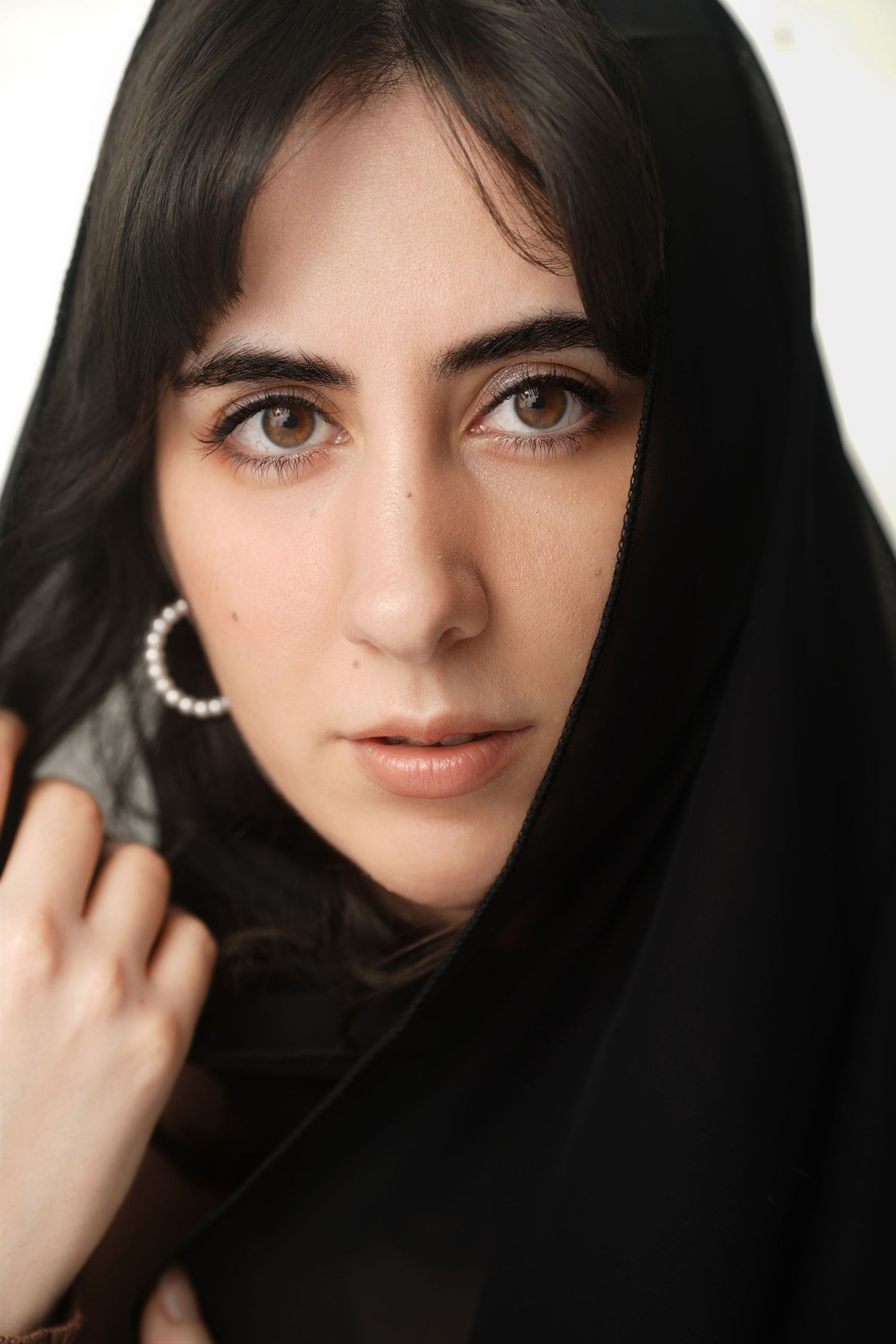 Close-up portrait of a woman with dark eyes wearing a black headscarf and silver hoop earrings.