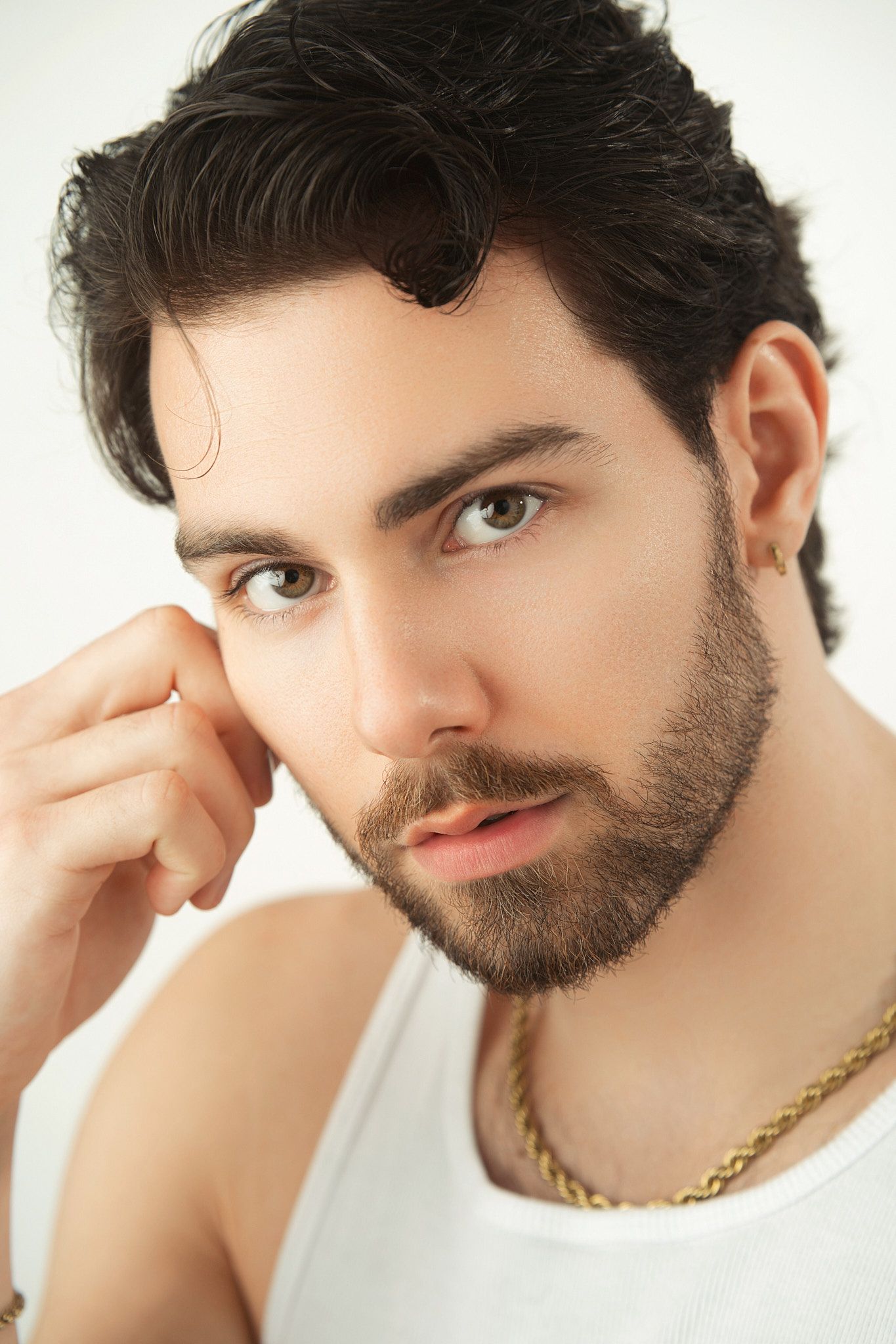 Close-up portrait of bearded man with dark hair wearing gold chain necklace and white tank top.