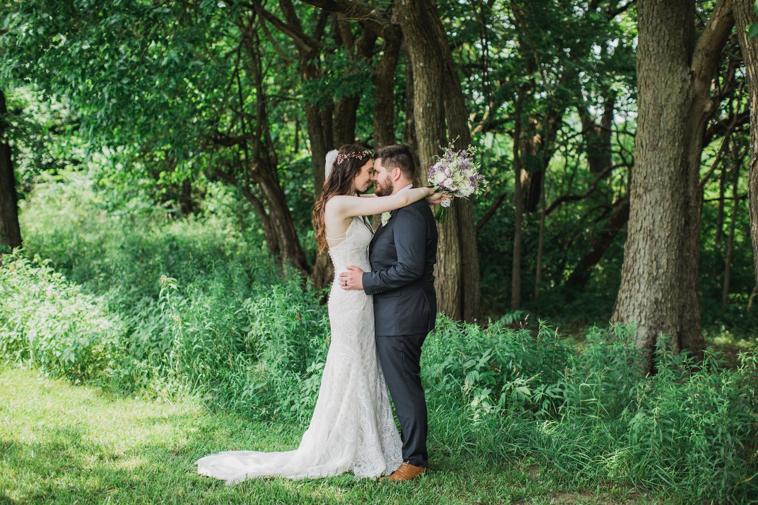 Bride and Groom at their wedding embracing in an outdoor scene holding bouquet of flowers.