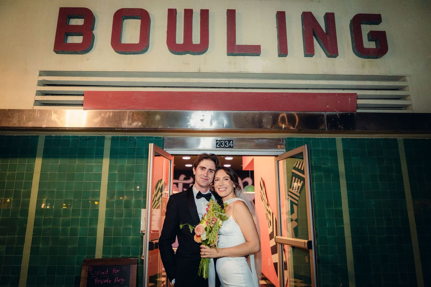 A couple poses outside a bowling alley reception party.