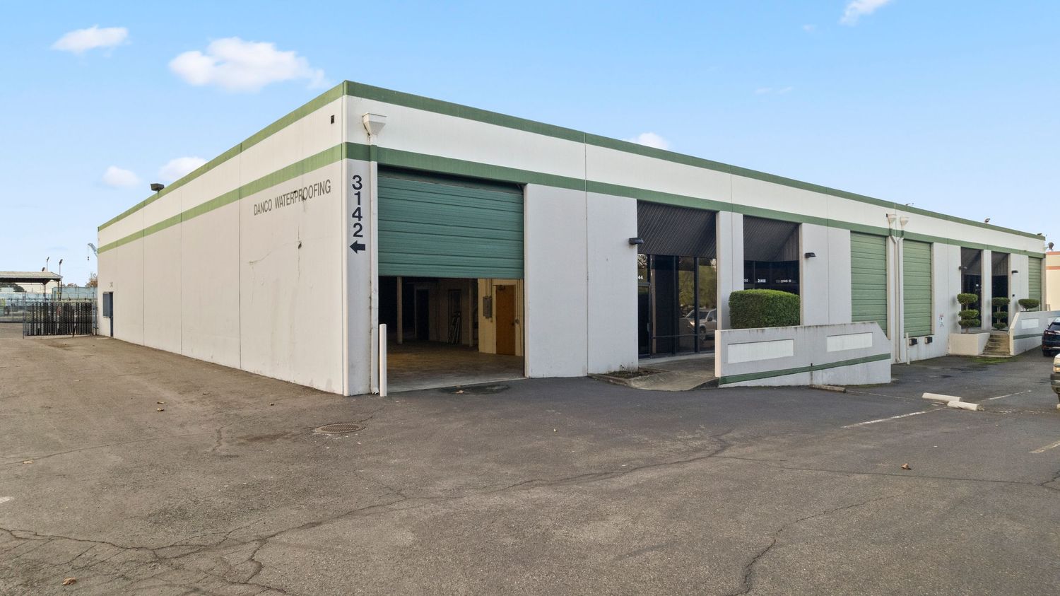Commercial warehouse building with green trim, roll-up doors, and paved parking lot.