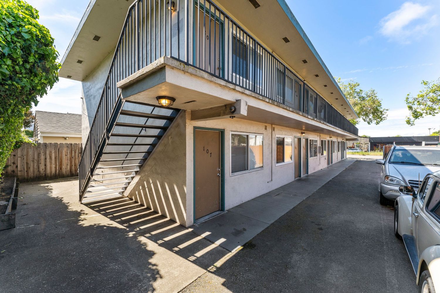 Two-story motel-style apartment complex with exterior staircase, open-air corridors, and parking lot in a suburban area.