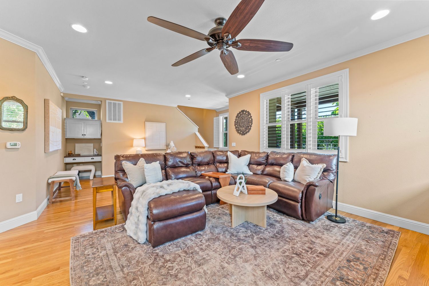 Spacious living room with brown leather sectional, ceiling fan, crown molding, and hardwood floors.