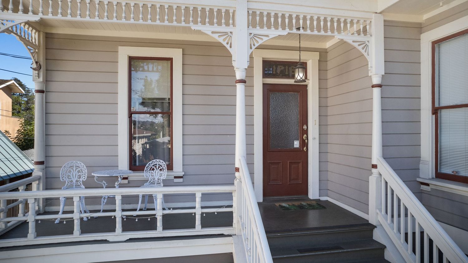 Charming Victorian home exterior with decorative porch railings, gray siding, and red front door.