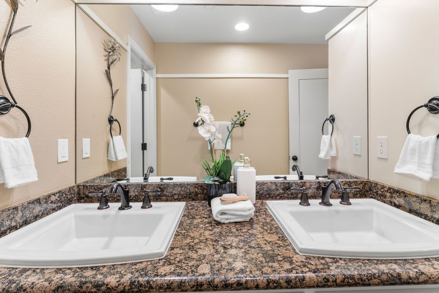 Elegant double-sink bathroom vanity with dark granite countertop, framed mirror, and white towels.