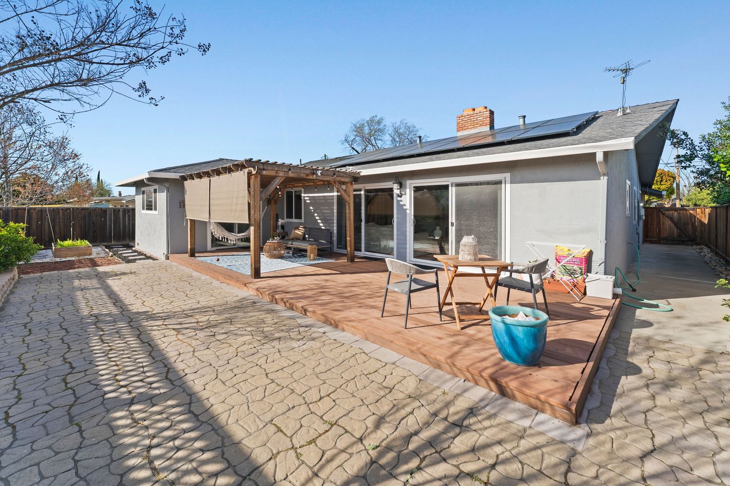 Ranch-style home exterior with solar panels, pergola, wood deck, and brick patio.