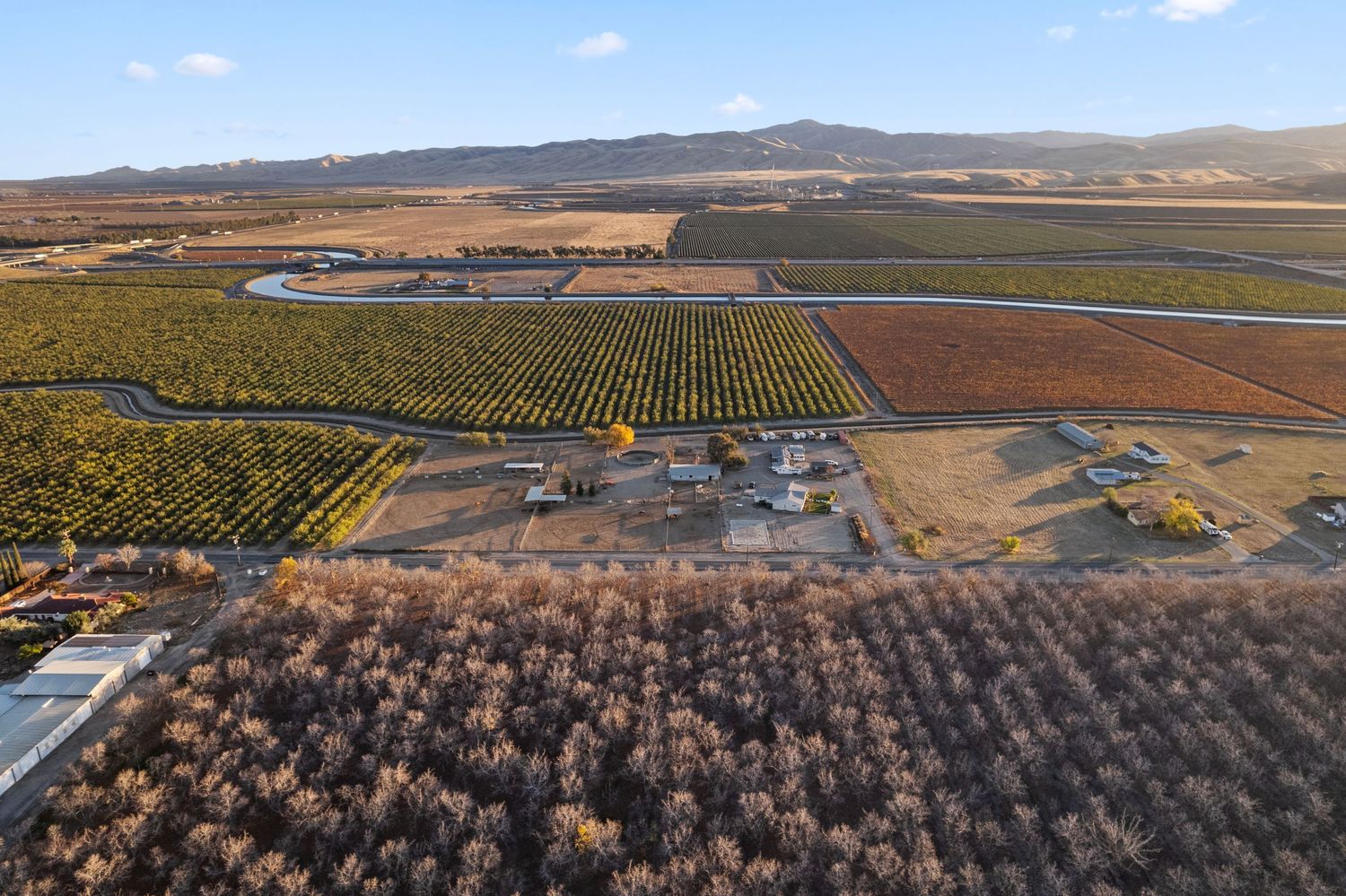 Aerial view of expansive agricultural farmland with orchards, vineyards, and mountain backdrop.