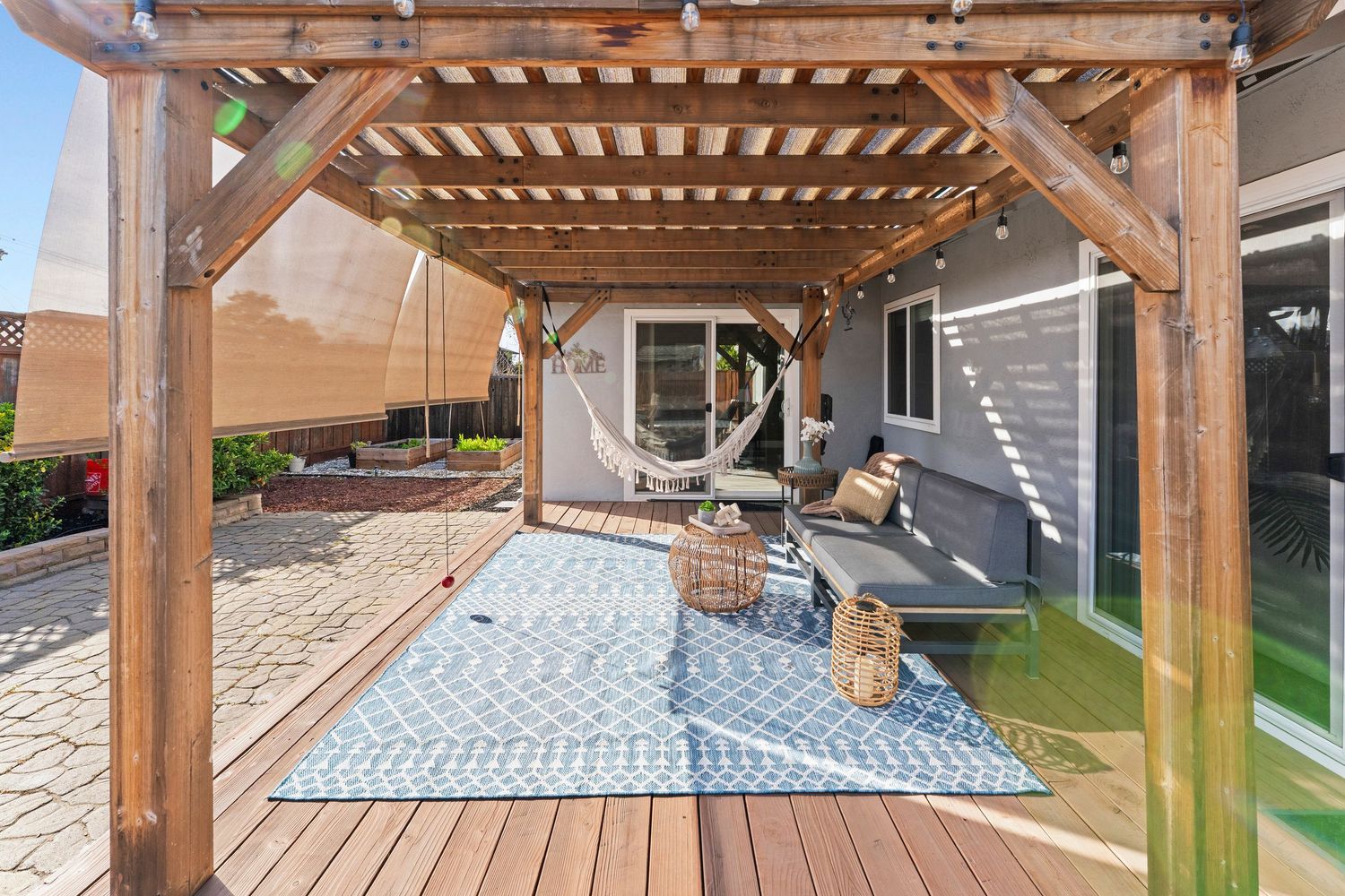 Shaded pergola with hanging hammock, outdoor rug, and wood deck in a private backyard.
