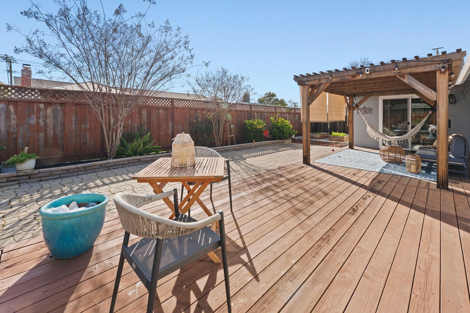 Spacious wood deck with pergola, outdoor dining set, and lush fenced backyard.