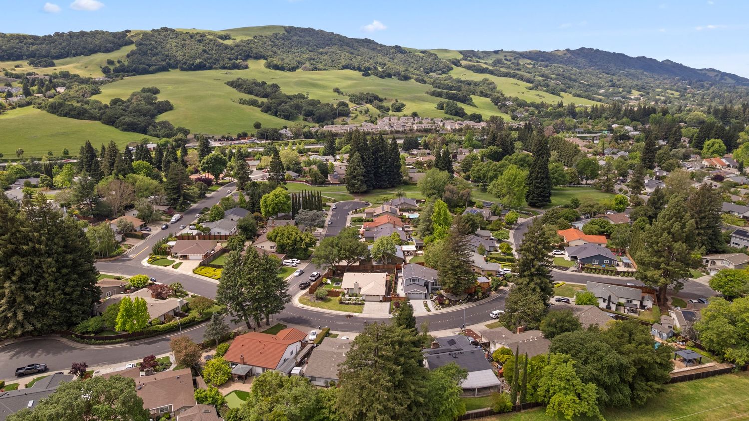 Aerial view of peaceful suburban neighborhood surrounded by lush green rolling hills.