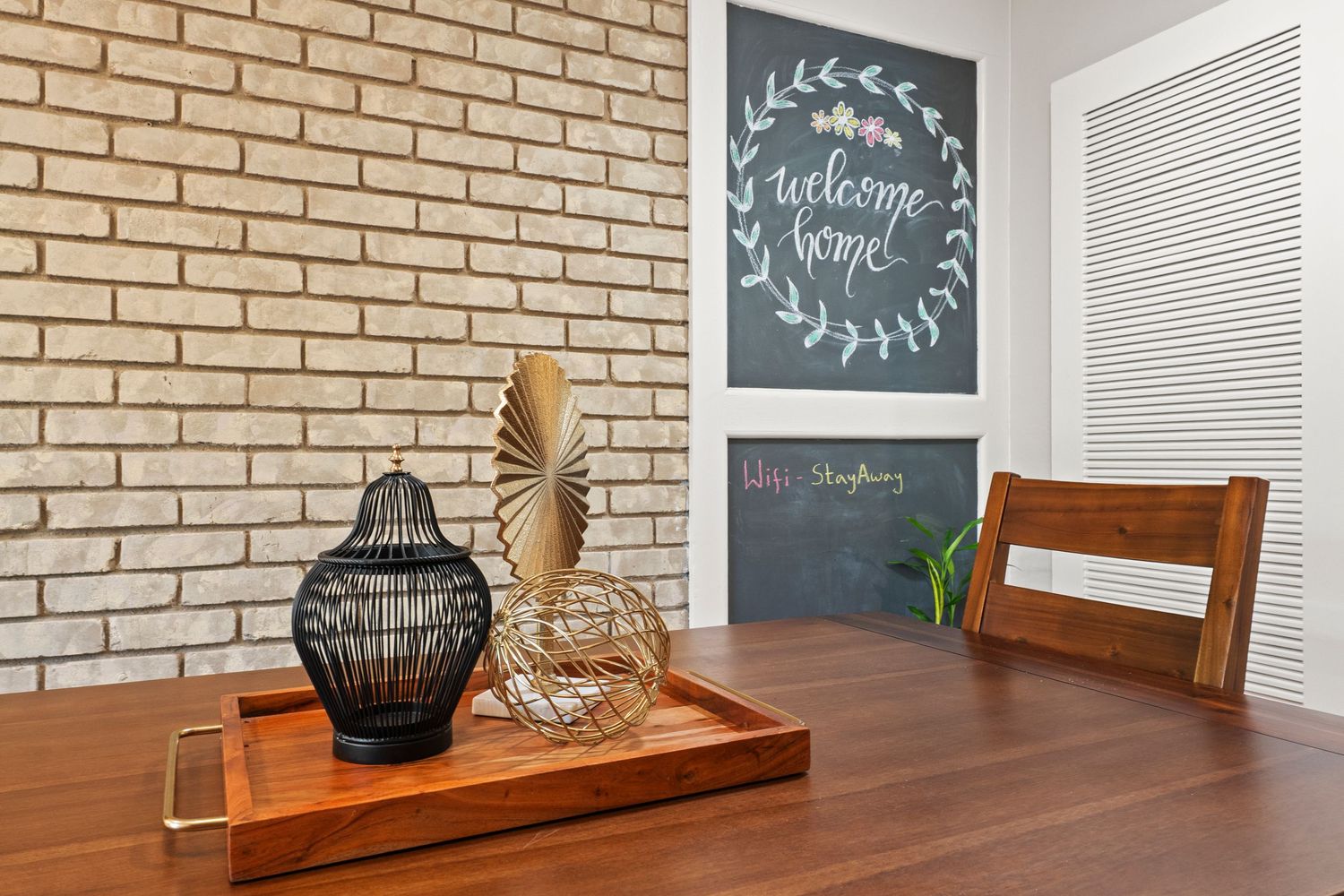 Dining area with wooden table, brick accent wall, and chalkboard welcome home sign.