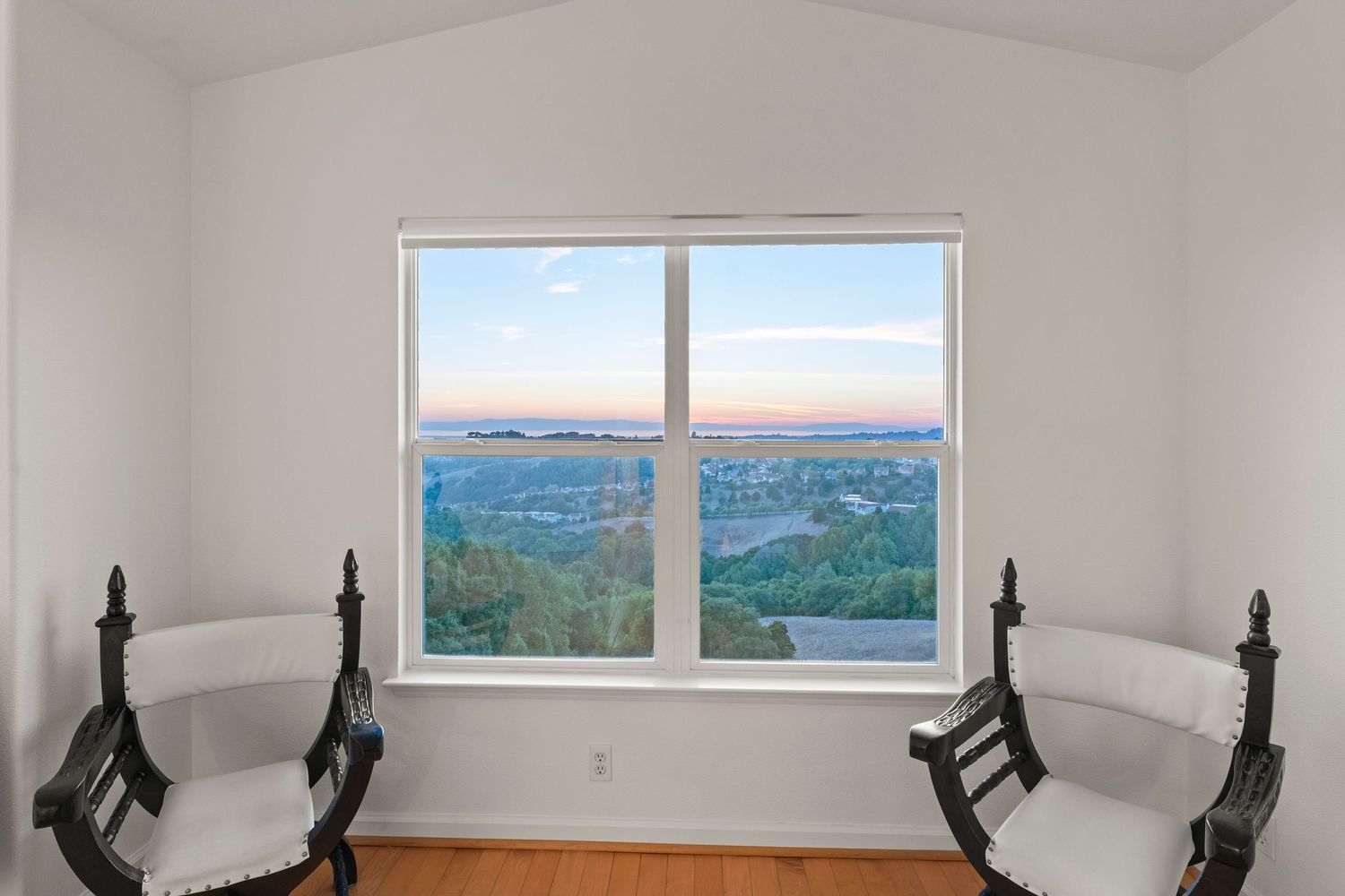 Serene sitting area with two antique chairs framing a large window with sunset views.
