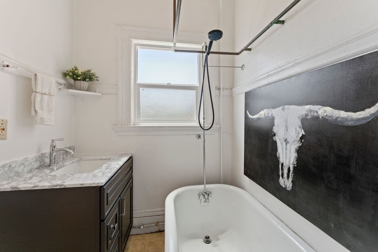Vintage bathroom with clawfoot tub, marble vanity, rain shower, and longhorn skull wall art.
