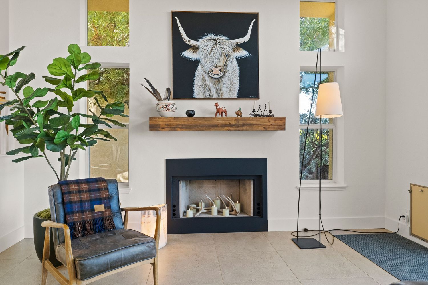 Cozy living room with modern fireplace, highland cow artwork, and fiddle leaf fig tree.