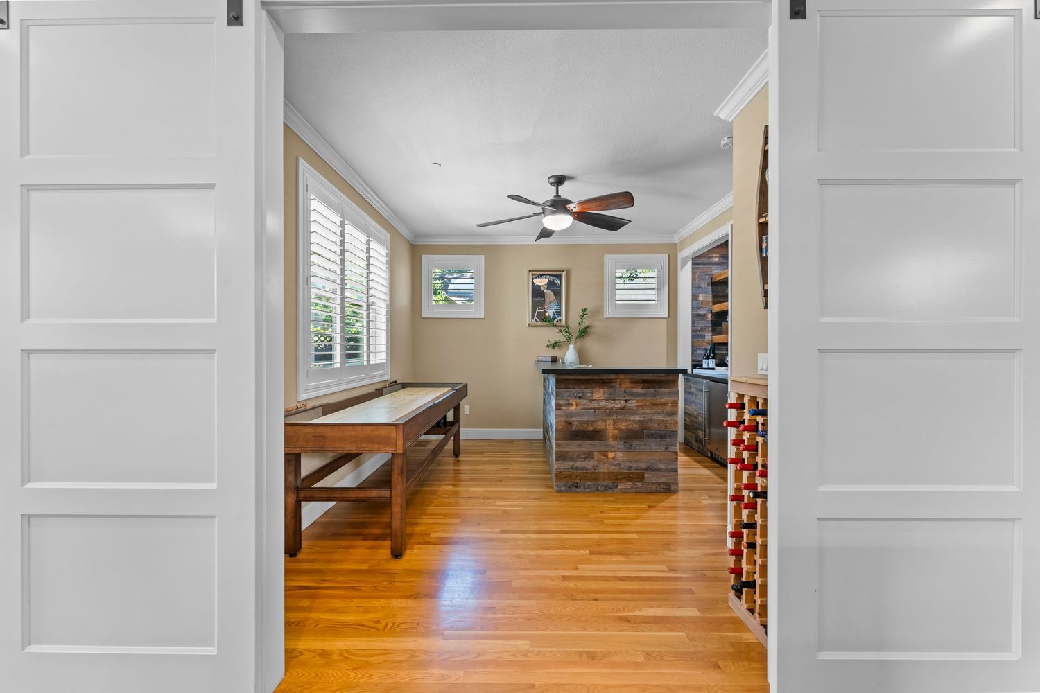 Game room with shuffleboard table, rustic bar, barn doors, ceiling fan, and hardwood floors.