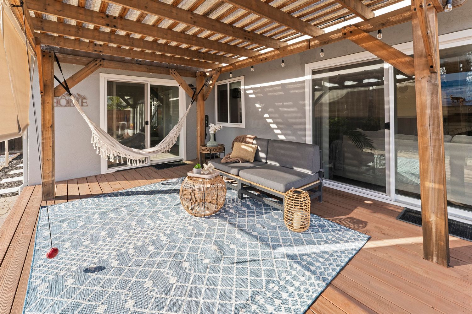 Outdoor deck with pergola, hammock, patio furniture, and blue geometric rug beside sliding glass doors.