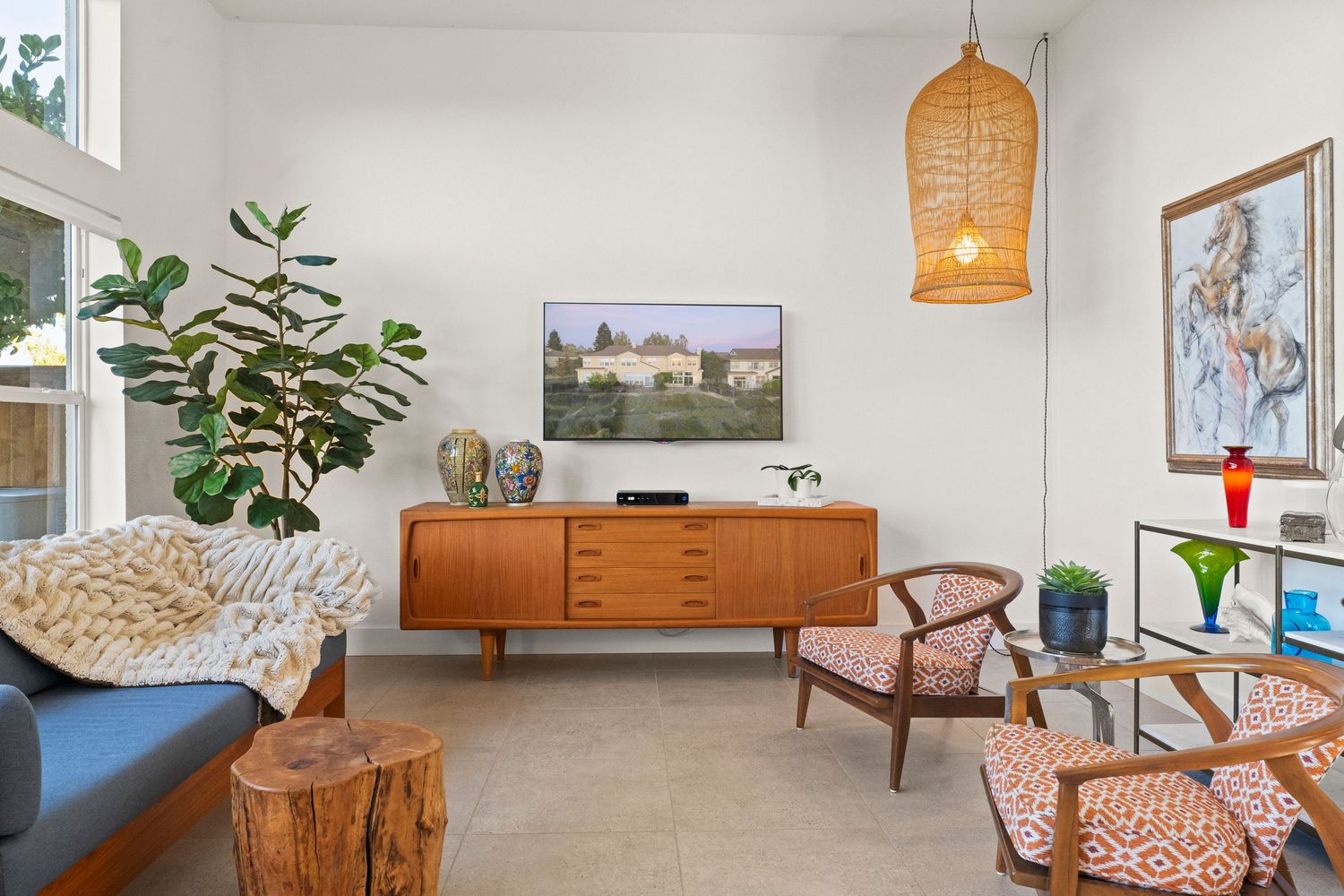 Mid-century modern living room with teak credenza, wicker pendant light, and fiddle leaf fig plant.