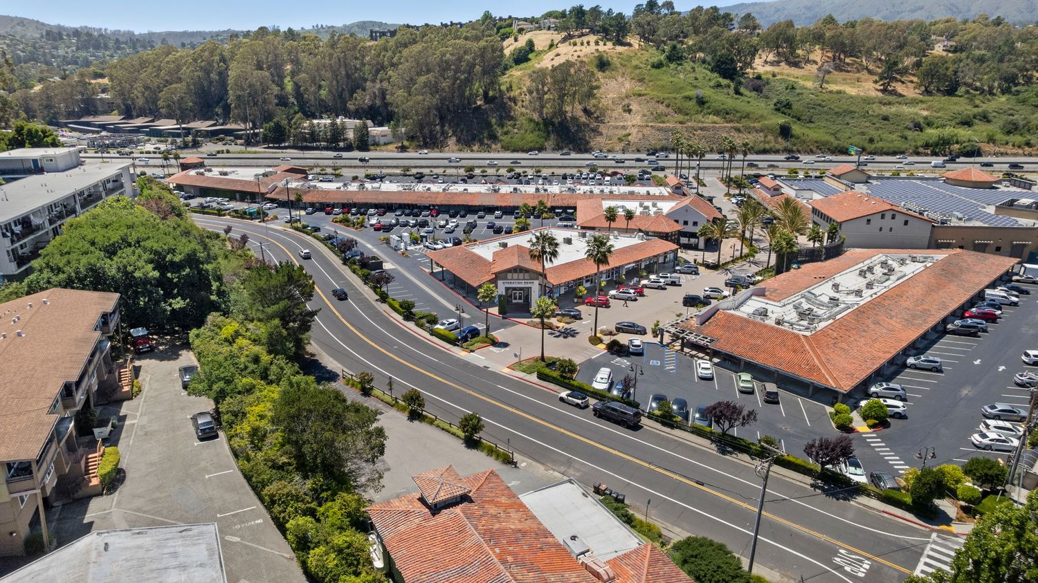 Aerial view of suburban shopping center with terracotta roofs and tree-lined streets.