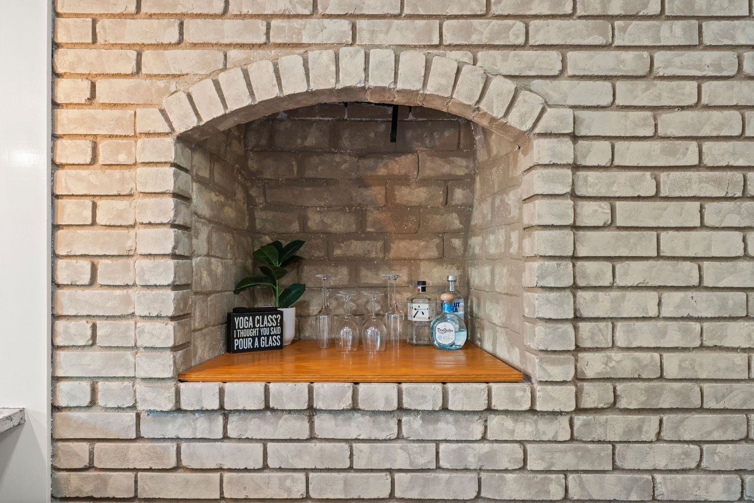 Rustic brick fireplace converted into a decorative bar shelf with glassware and bottles.