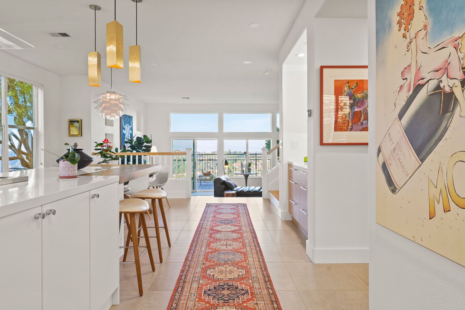 Bright white kitchen hallway with pendant lights, marble countertop, runner rug, and stunning ocean view beyond.
