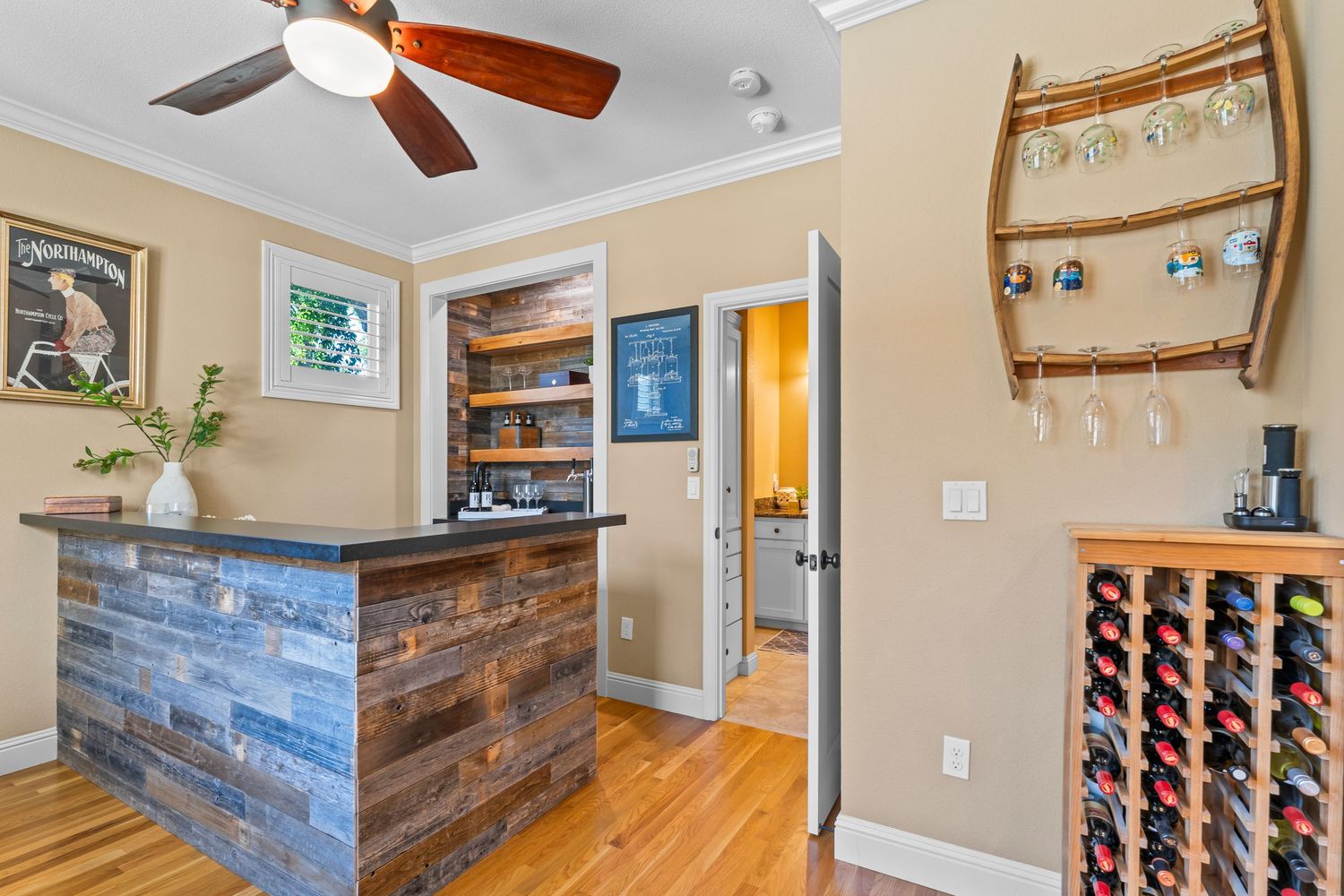 Rustic home bar with reclaimed wood paneling, built-in shelving, wine rack, and ceiling fan.